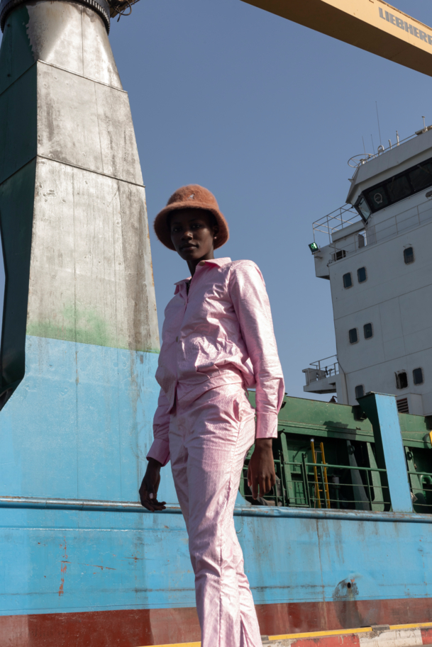 Model in pink suit posing in front of a container ship