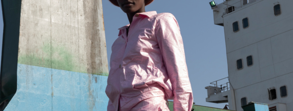 Model in pink suit posing in front of a container ship