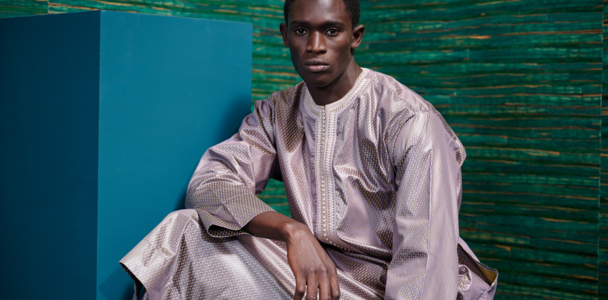 Man in mauve Boubou sitting in front of a green-blue wallpaper